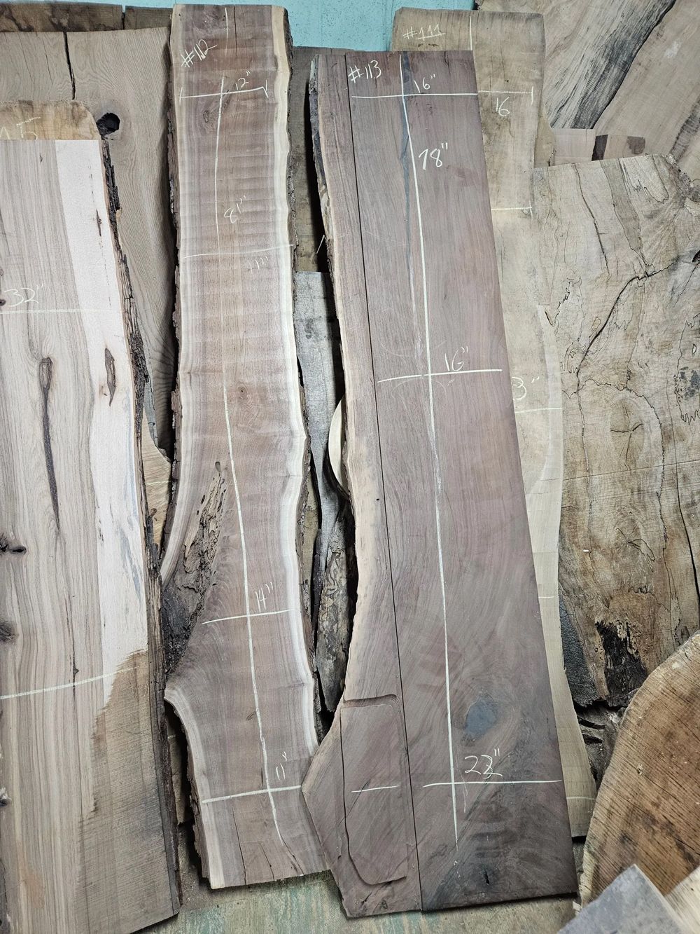 Wooden slabs with natural edges and marked measurements in a workshop setting.