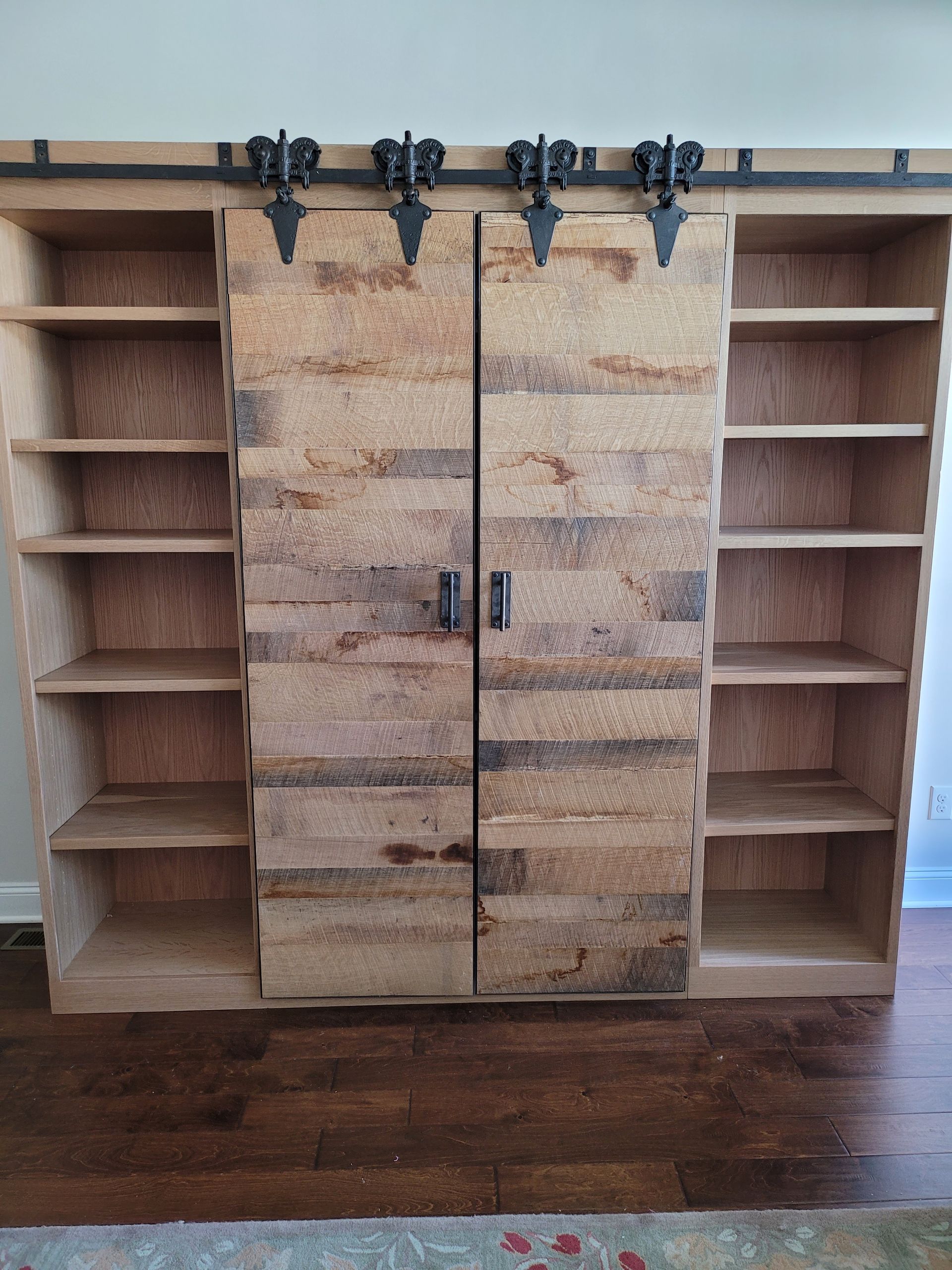 A wooden bookshelf with sliding barn doors in a living room.