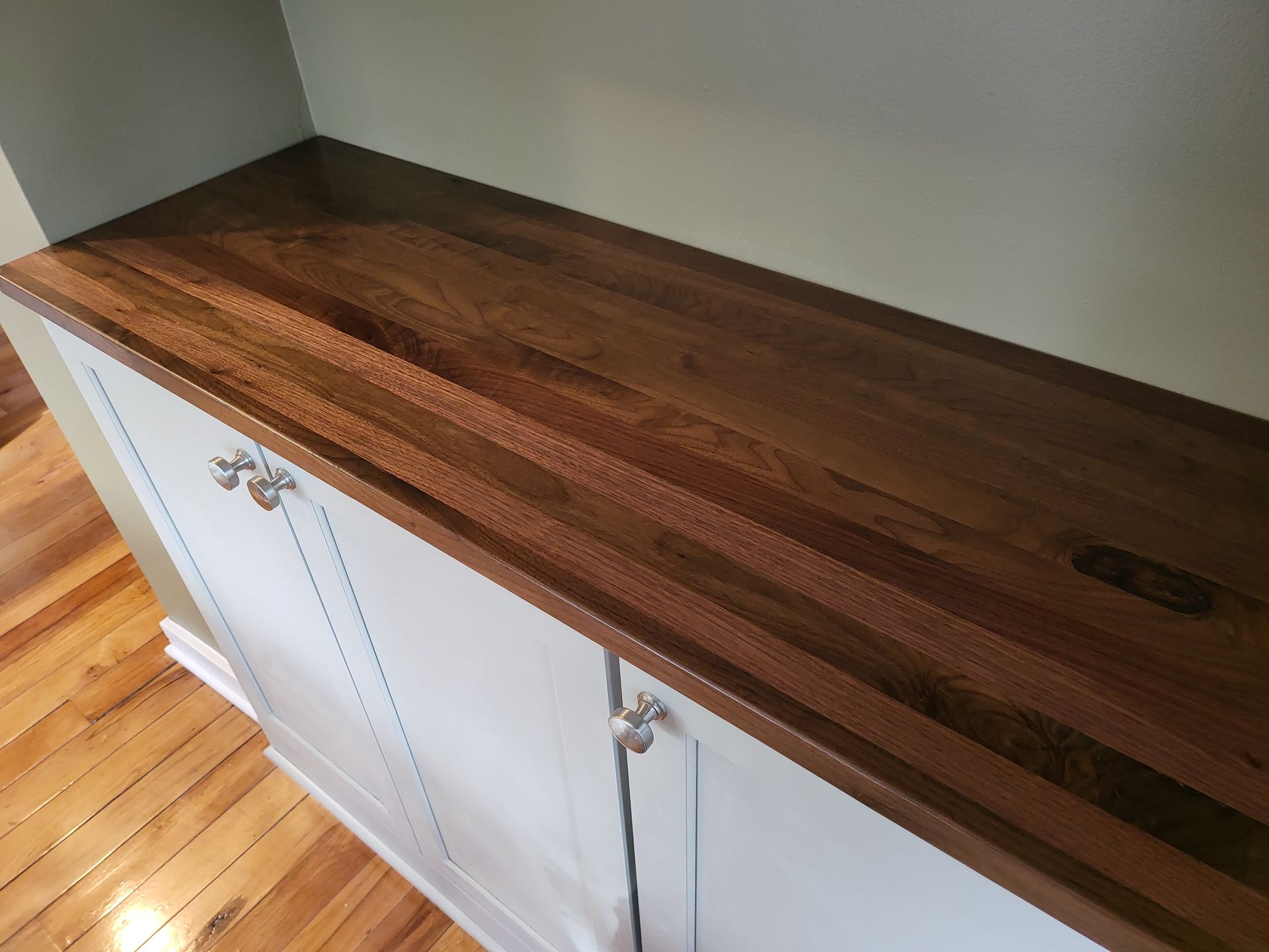 A wooden counter top with white cabinets in a kitchen.