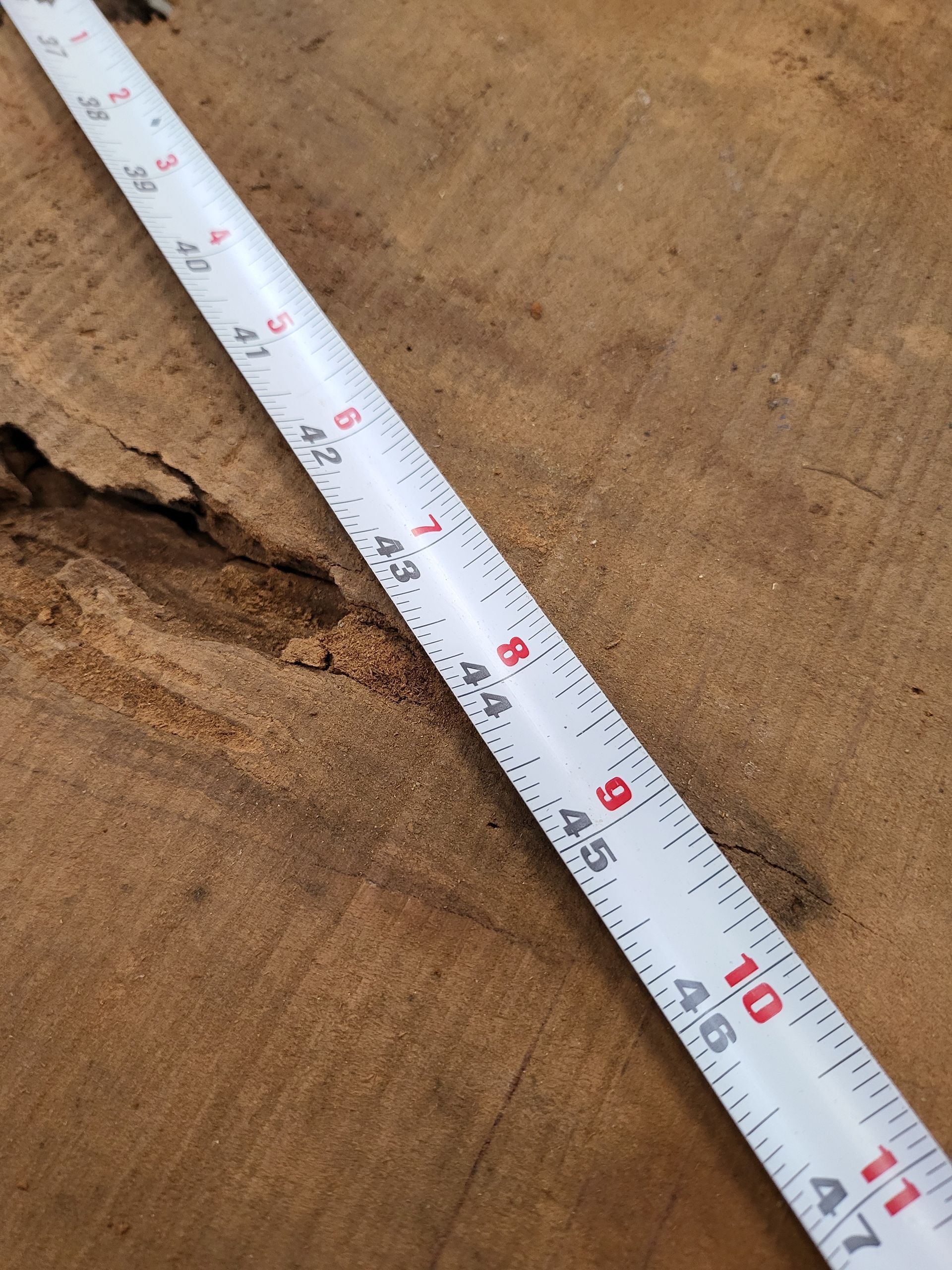 A white tape measure is laying on a piece of wood