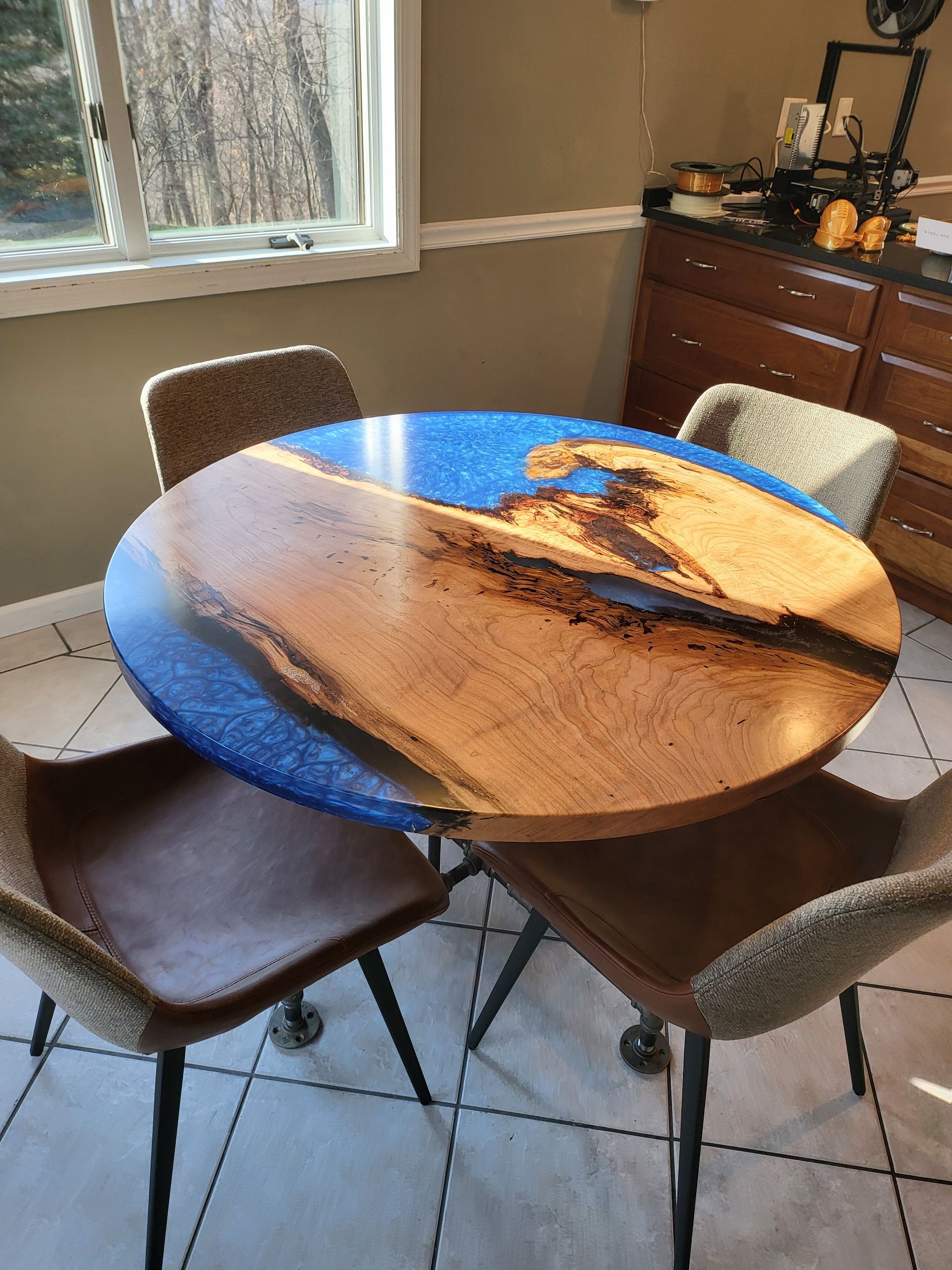 A round wooden table with a blue top and four chairs in a dining room.