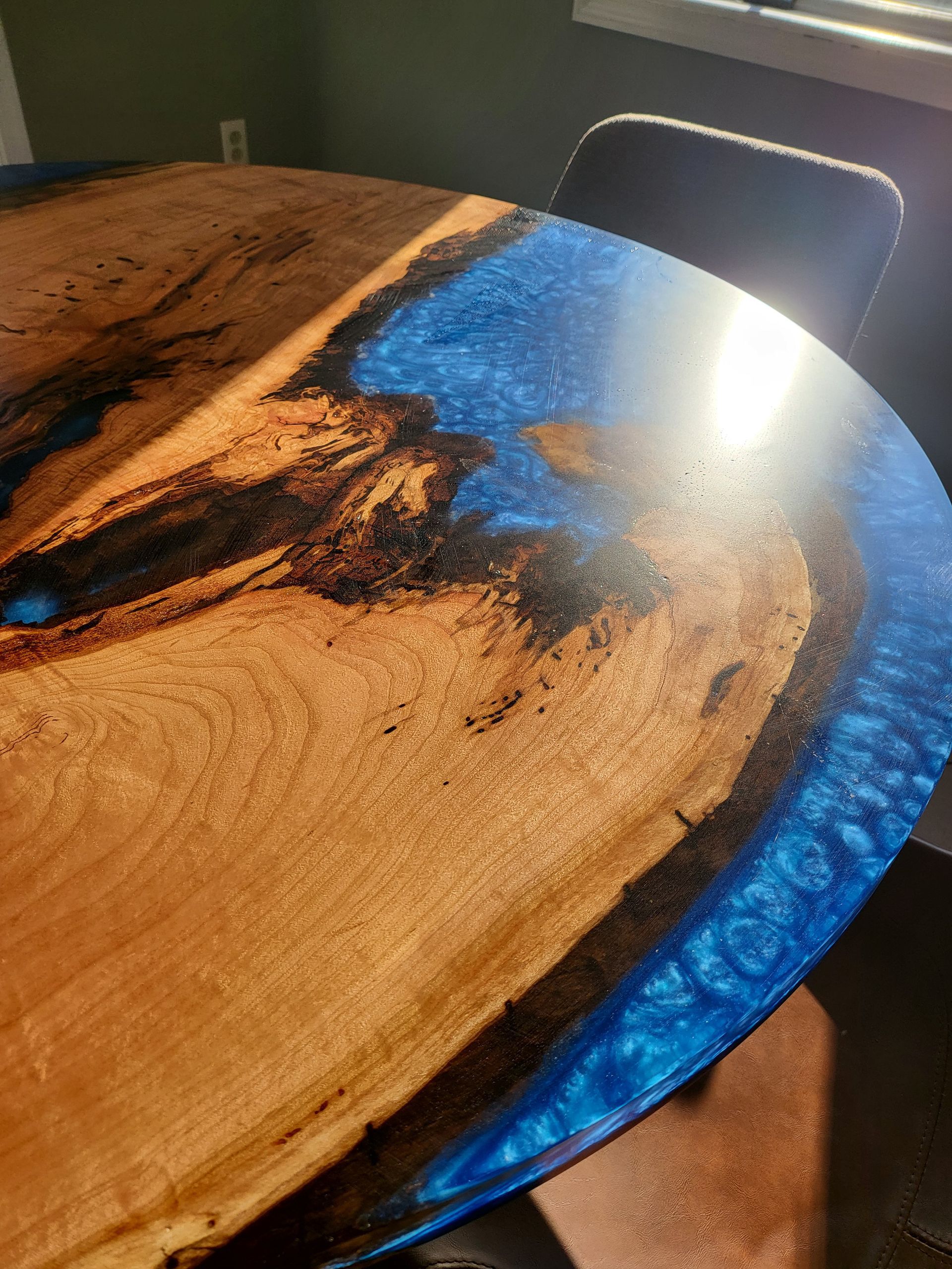 A person is holding a wooden table with blue resin on it.