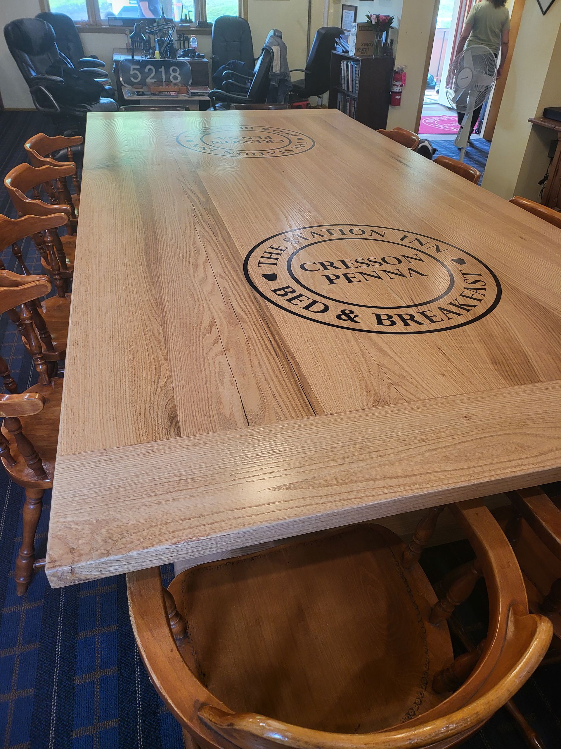 A wooden table with a logo on it is in a room with chairs.