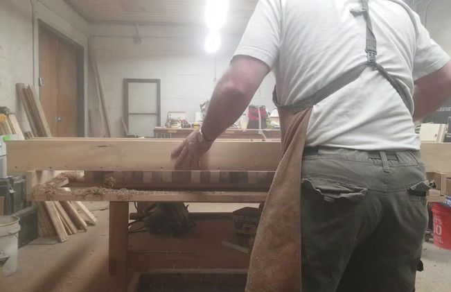 A man wearing an apron is working on a piece of wood in a workshop.