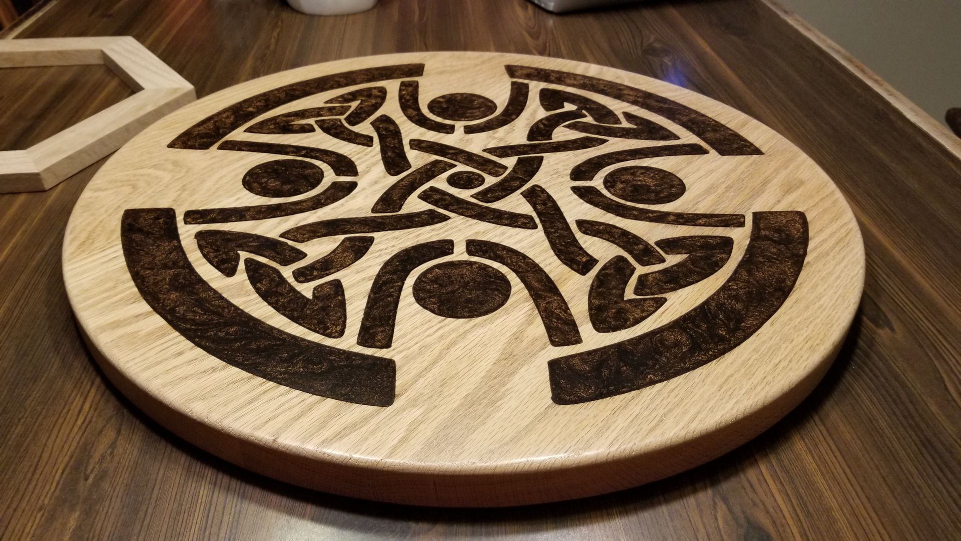 A wooden cutting board with a celtic design on it is sitting on a wooden table.