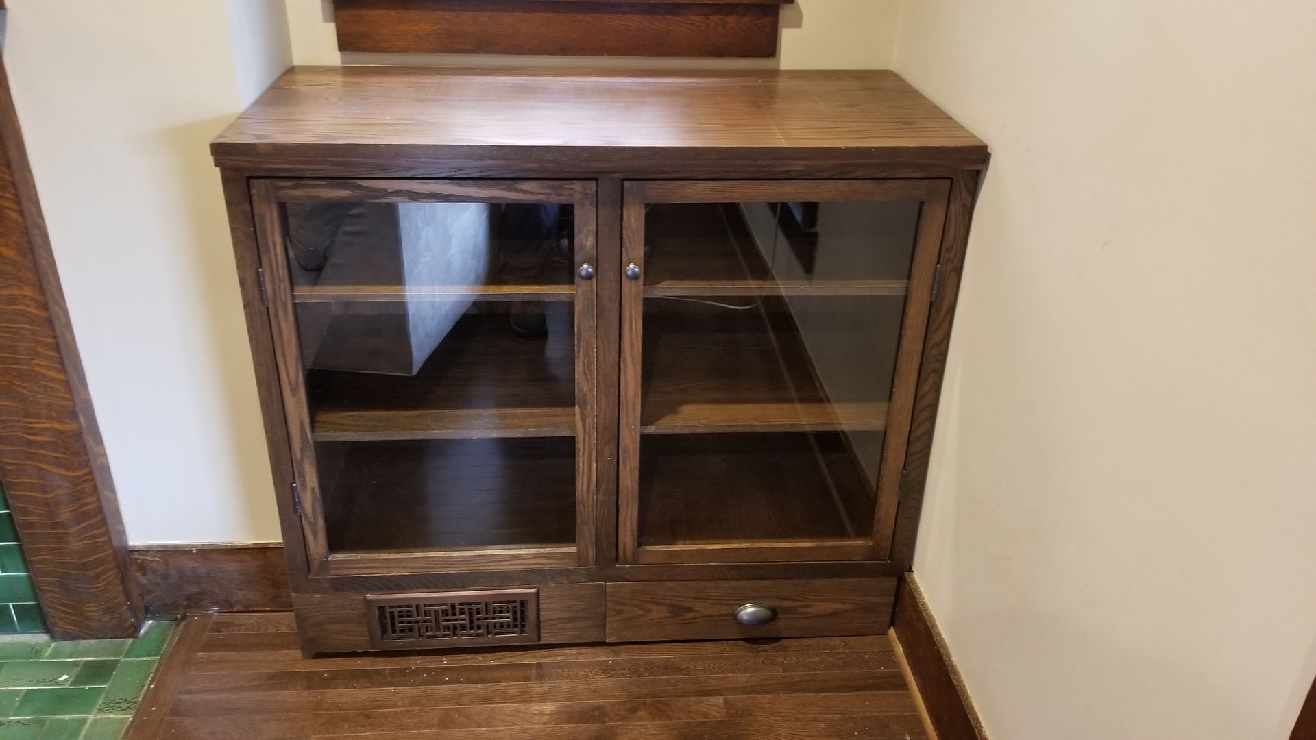 A wooden cabinet with glass doors and drawers in a hallway.