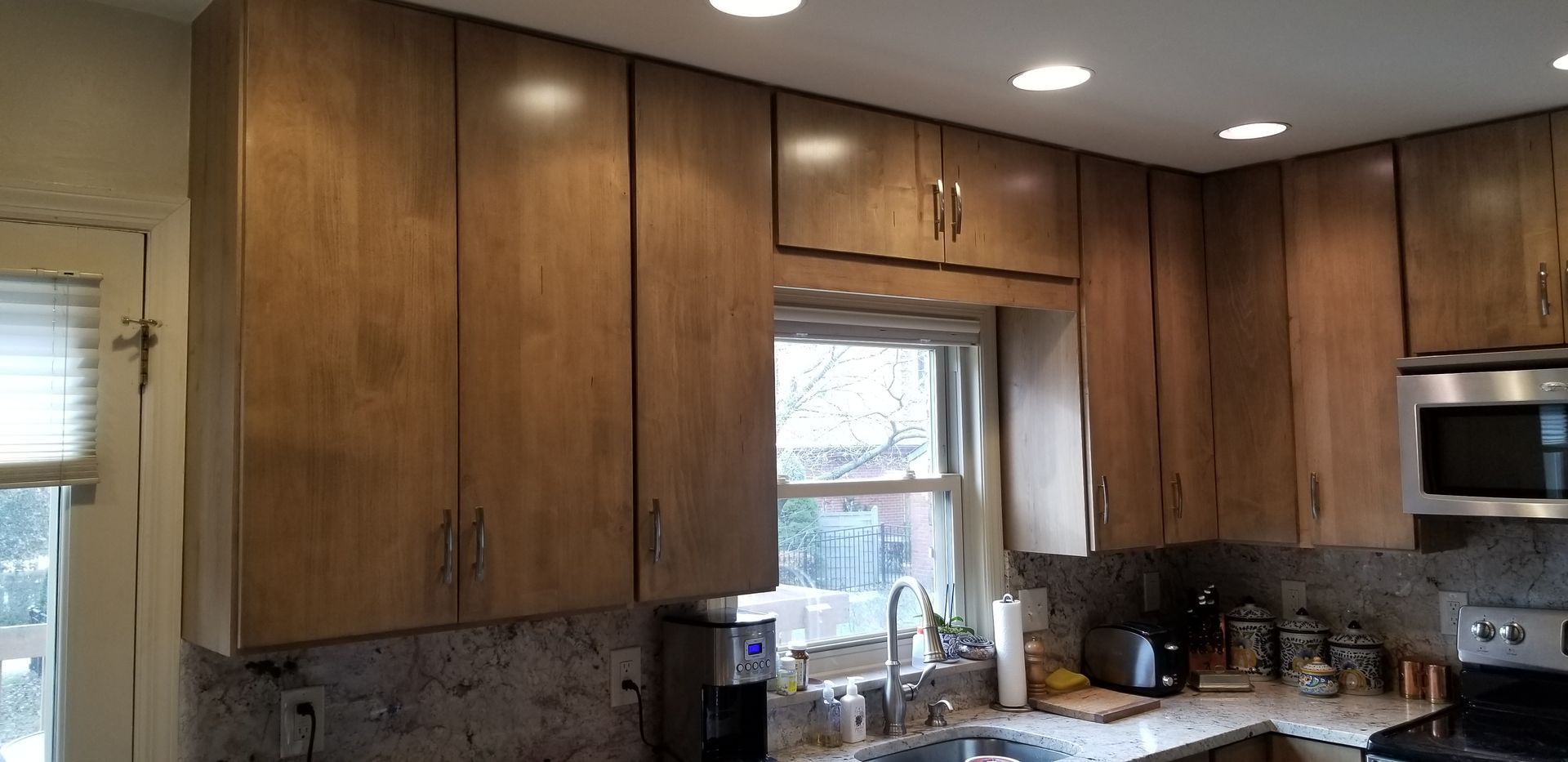 A kitchen with wooden cabinets , a sink , a microwave , and a window.