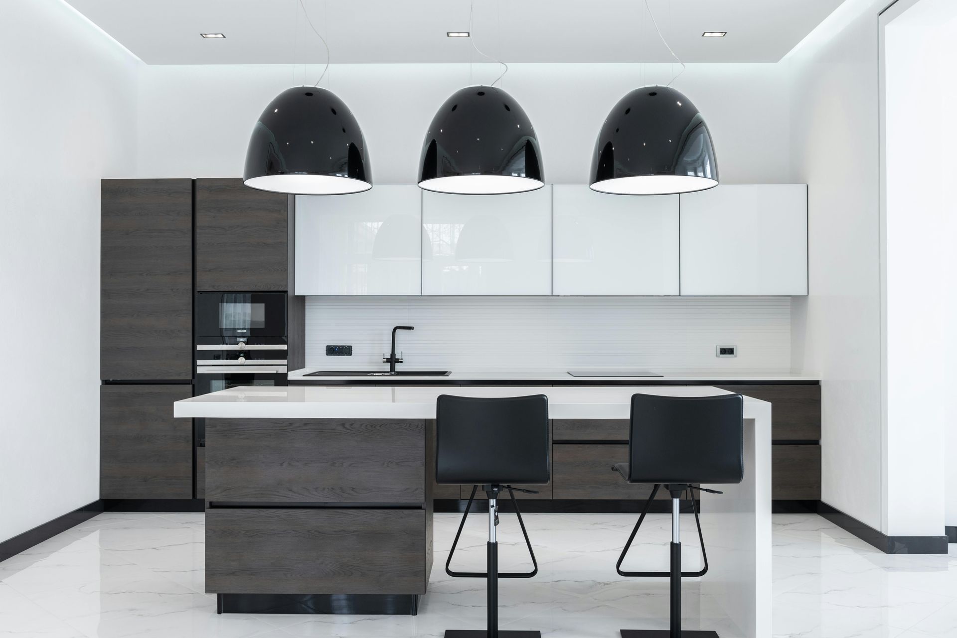 Modern kitchen with dark wood cabinets, white countertops, black pendant lights, and two bar stools.