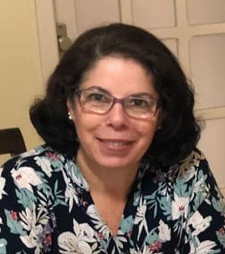 Uma mulher usando óculos e uma blusa florida está sorrindo para a câmera.