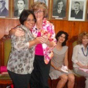 Duas mulheres estão se abraçando na frente de um grupo de pessoas sentadas em cadeiras.