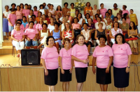 Um grupo de mulheres com camisas rosas estão em pé na frente de um alto-falante