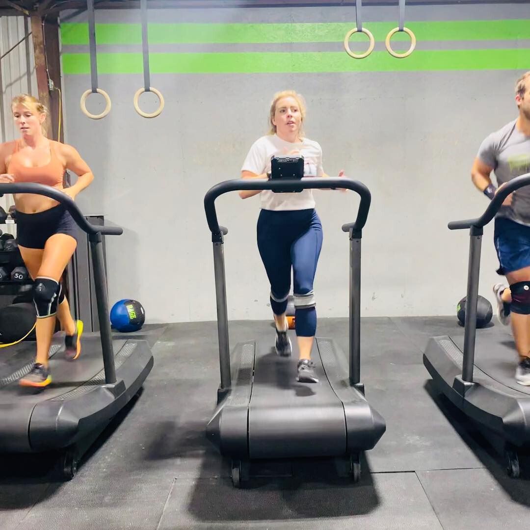 Three people are running on treadmills in a gym