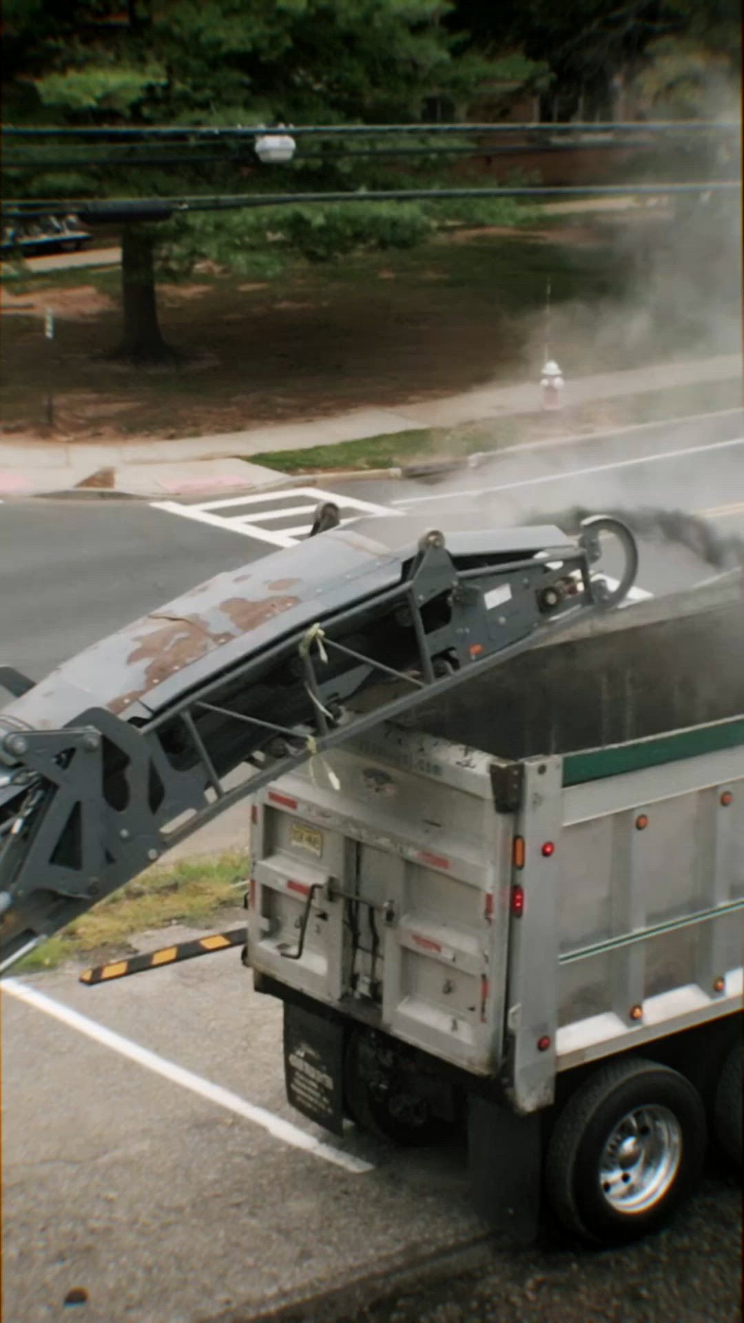 A dump truck is being loaded with a machine on the side of the road.