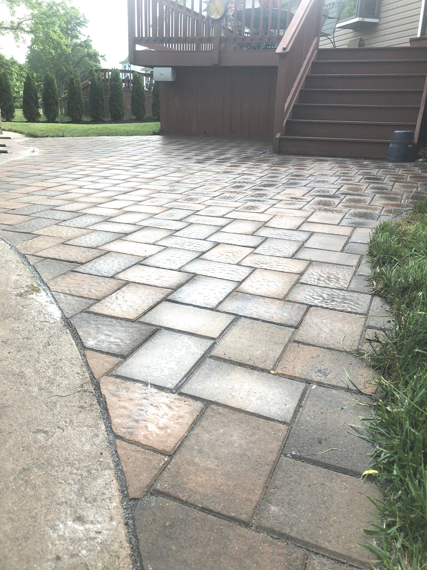 A brick patio with a deck and stairs in the background.