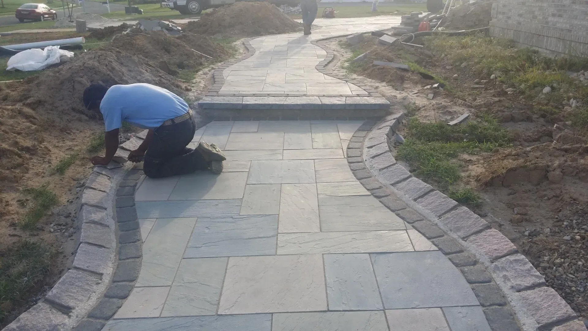 A man is kneeling down on a brick walkway.