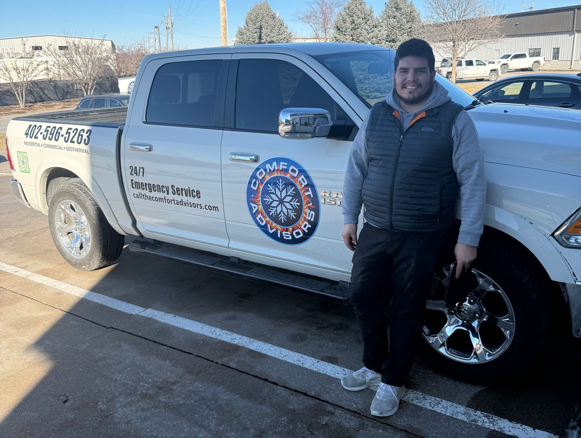 Man standing next to a white pickup truck with company logo. Sunlit parking lot setting.