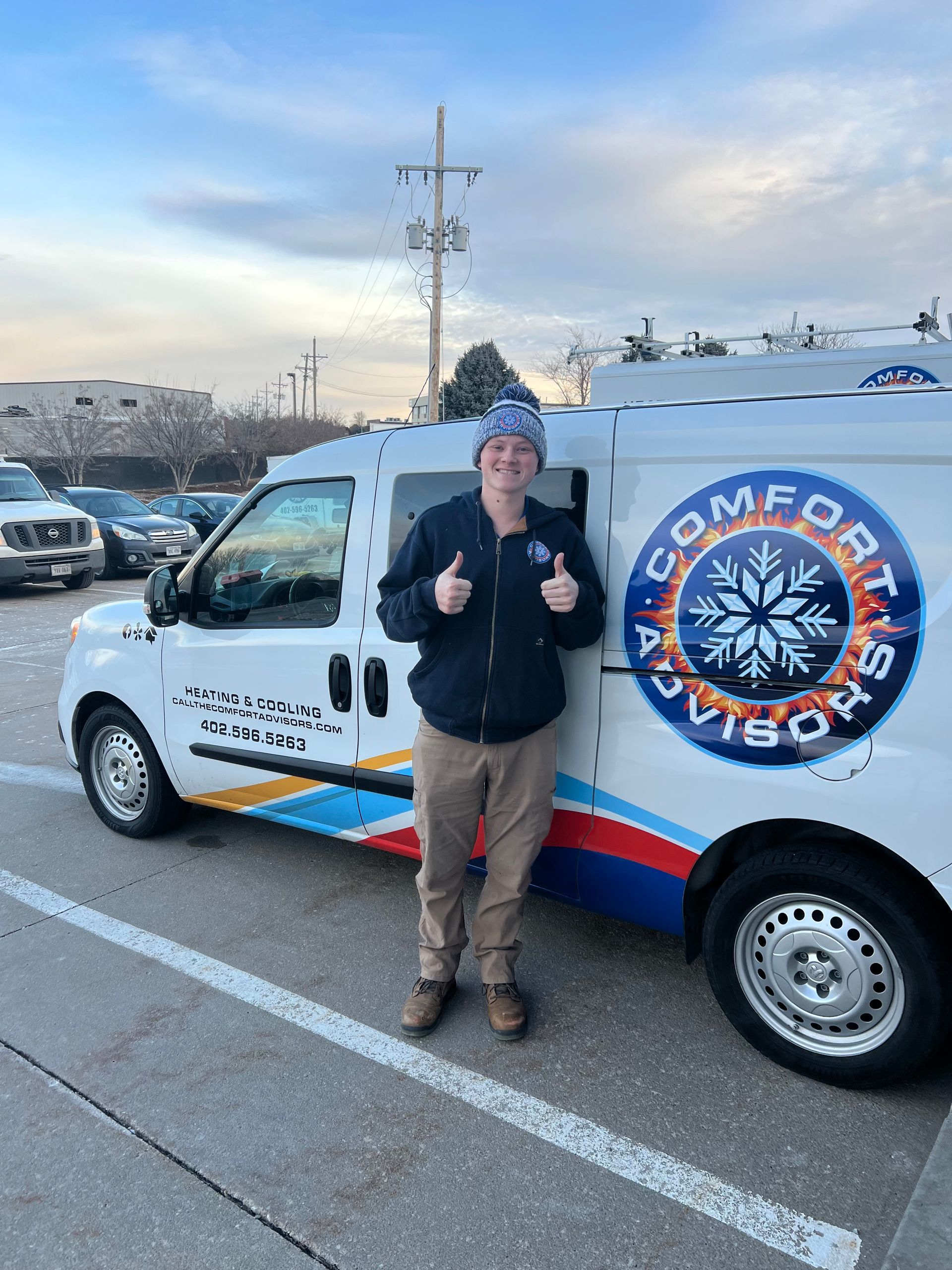 Person standing by a Comfort Advisors van, giving thumbs up. Cloudy sky, parking lot setting.