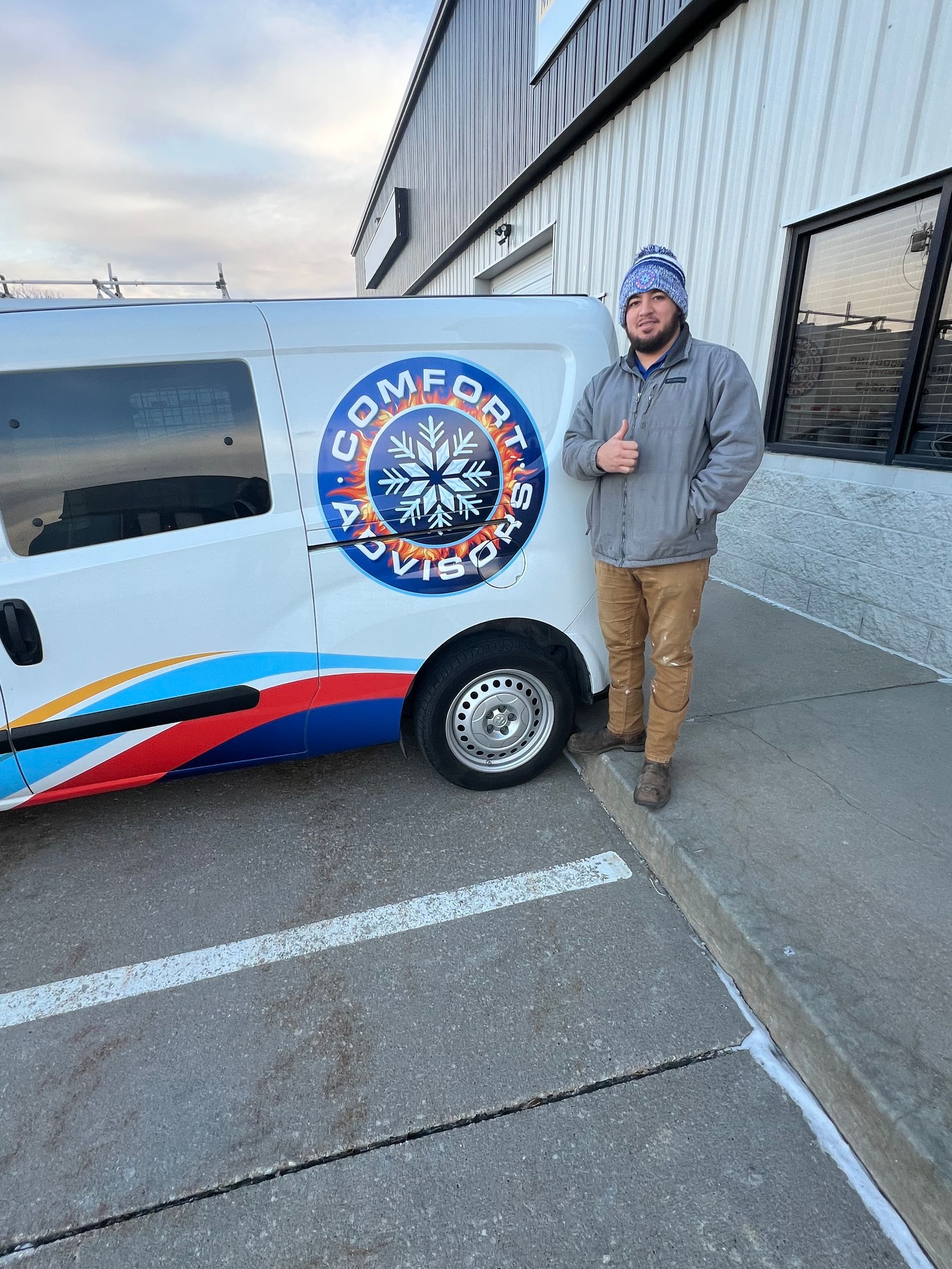 Man in front of HVAC van, giving a thumbs up. Van has company logo. Gray jacket and brown pants.