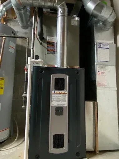 A furnace and water heater in a basement setting. The furnace is black and gray with a vent.