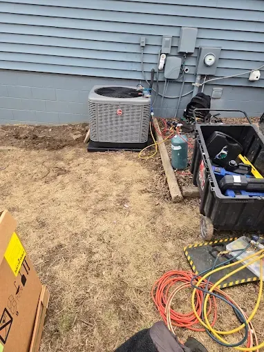 HVAC unit outside a blue-sided building. Equipment and tools are scattered on the ground.