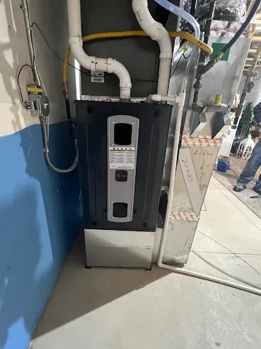 Furnace against a blue and gray wall. White pipes, metal casing, and a person in the background.
