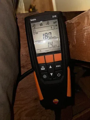 Testo 310 combustion analyzer reading 180 and 14 in an unknown setting, held by a person.