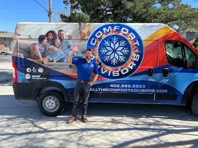Man in blue shirt waves next to a Comfort Advisors van with family graphic and logo.