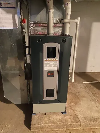 Dark gray furnace in a basement setting with air ducts.