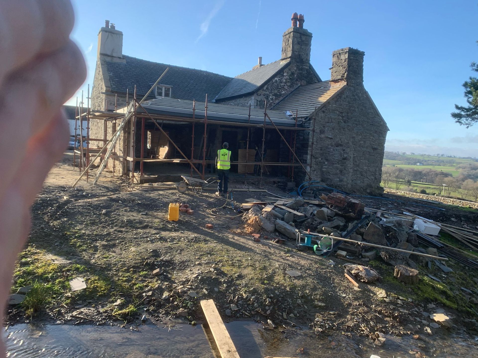 A man in a yellow vest is standing in front of a large stone building under construction.