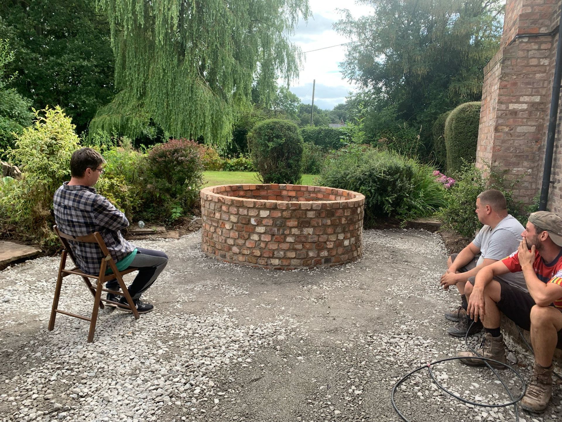 A group of men are sitting around a brick fire pit.