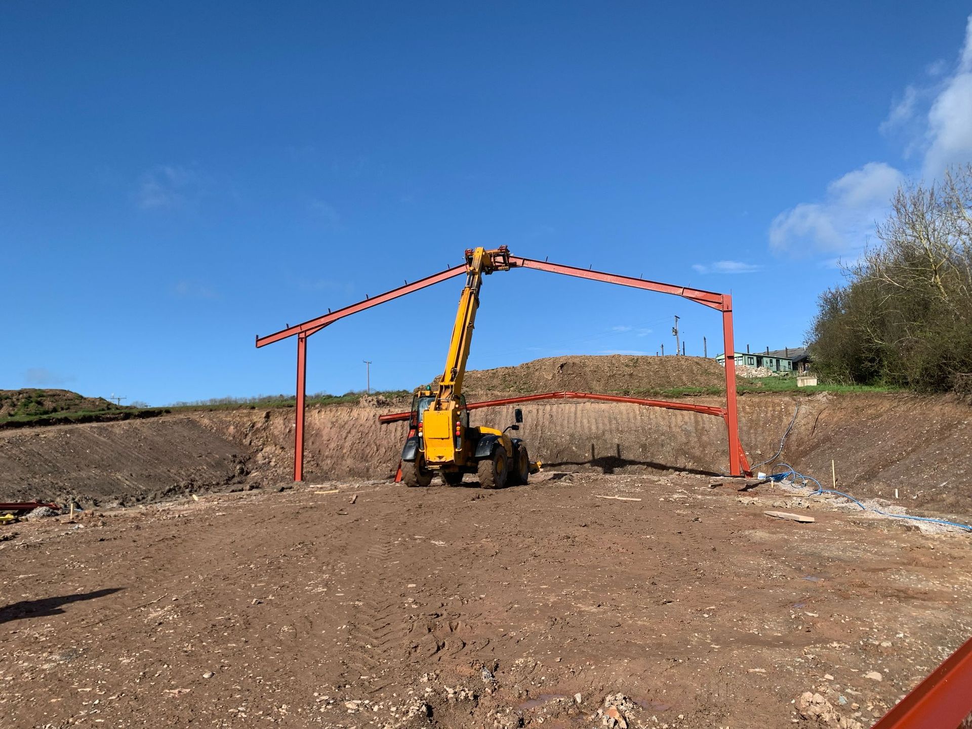 A yellow crane is lifting a metal structure in a dirt field.