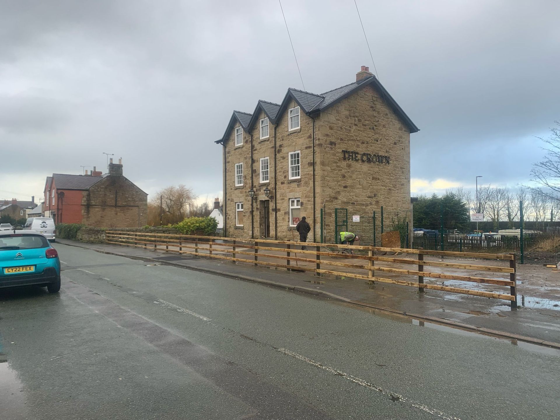 A blue car is parked on the side of the road in front of a large stone building.