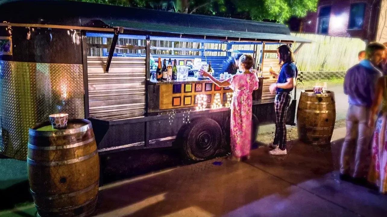 A woman in a pink dress is standing in front of a food truck.