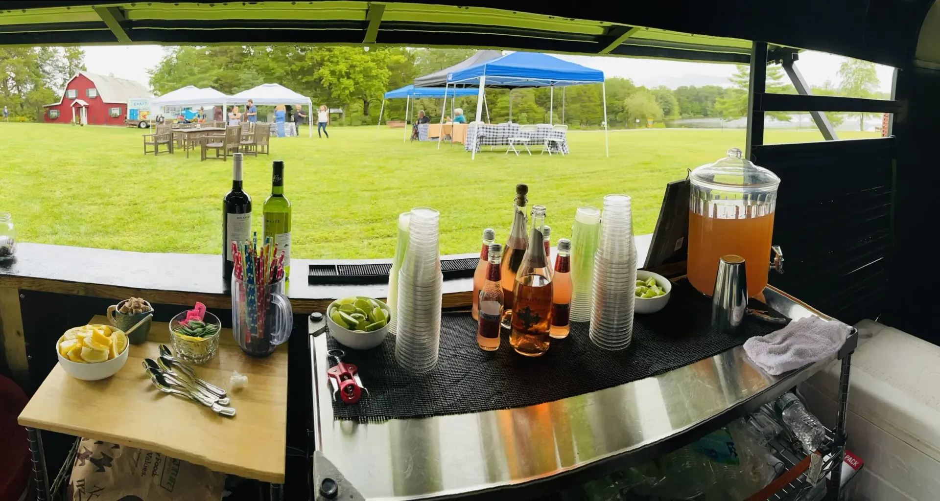 A table with bottles of wine and drinks on it and a view of a field.