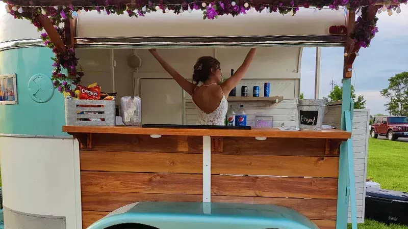 A woman is standing in front of a food truck with her arms outstretched.