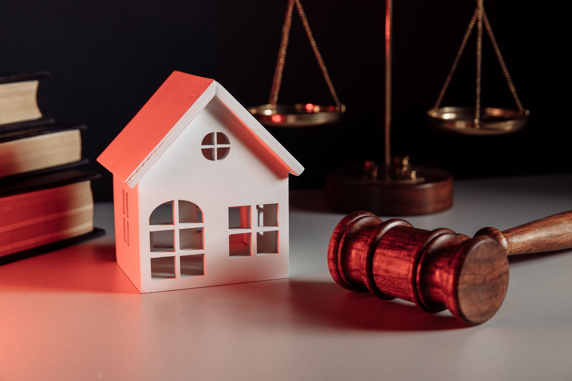 A model house, a wooden gavel, and a balance scale sit next to a stack of books, representing real estate law.