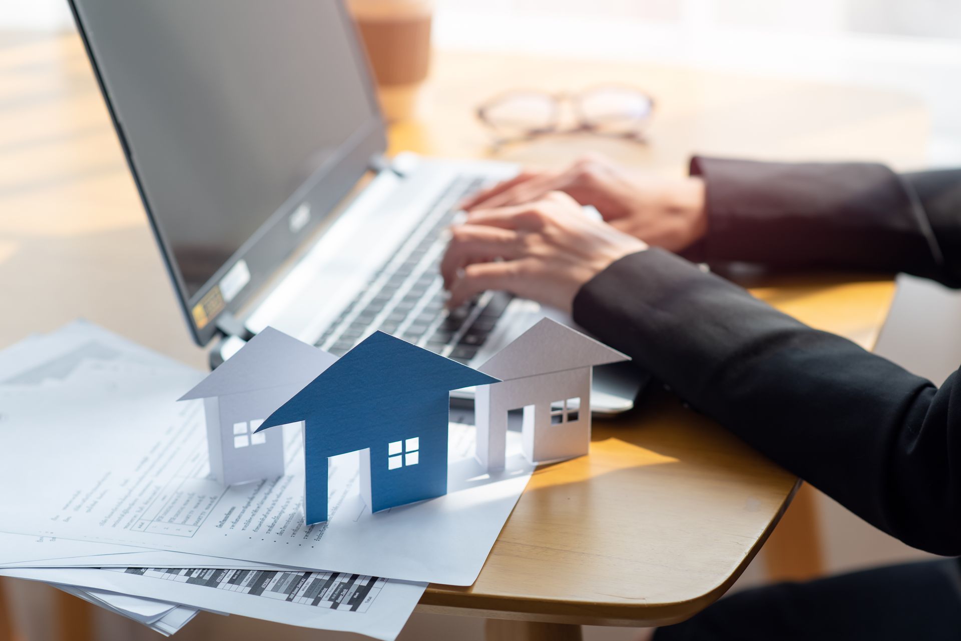 Person typing on laptop, miniature houses on a desk with paperwork.