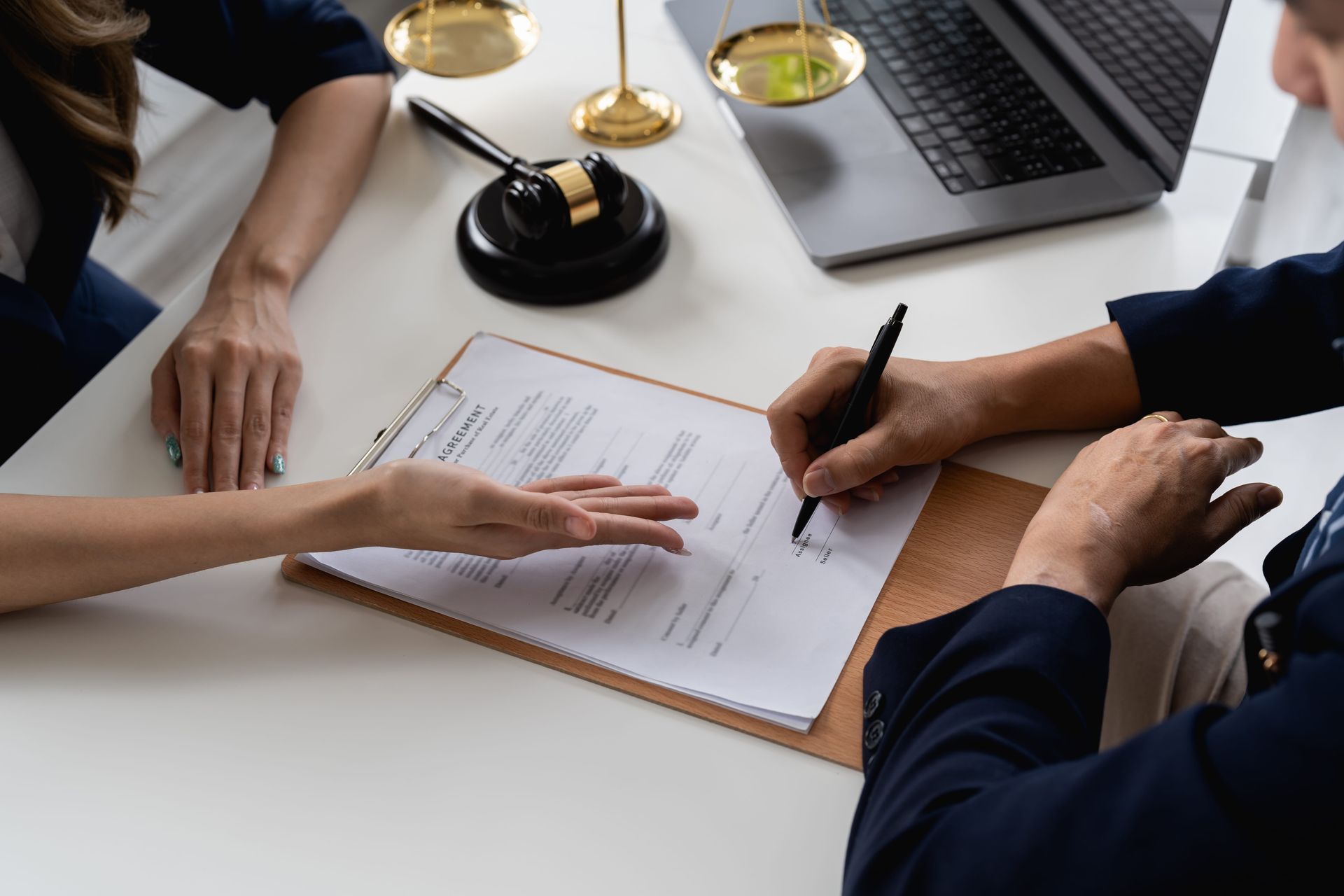 Hands reviewing and signing a document at a desk with laptop and scales of justice