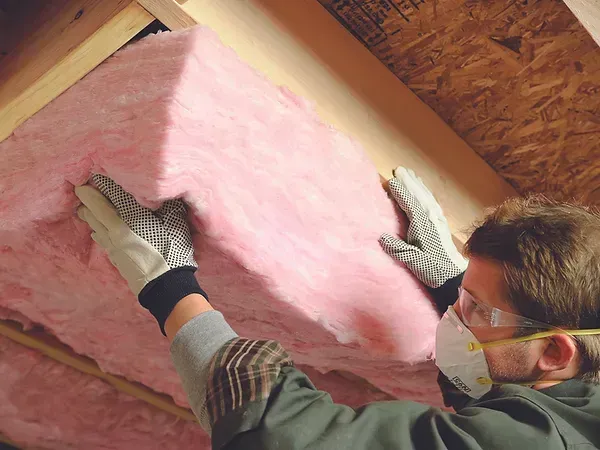 A man wearing a mask and gloves is holding a piece of pink insulation.