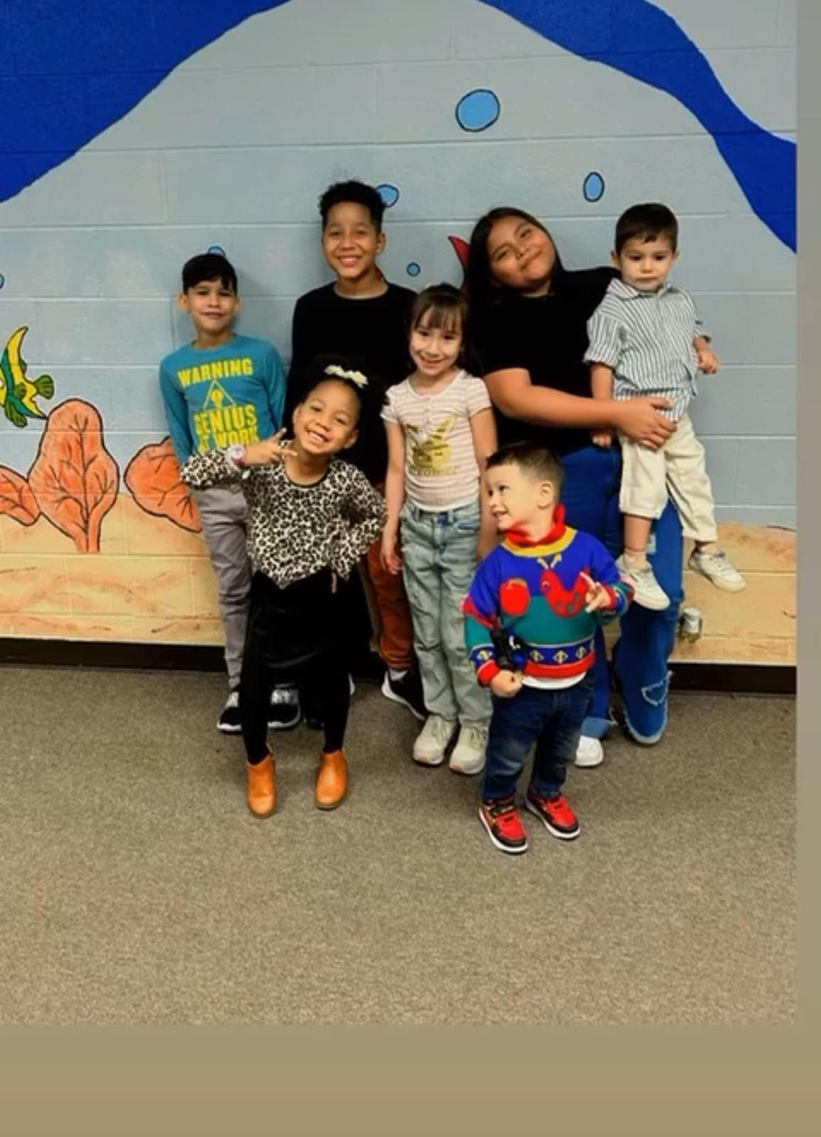 Group of children smiling near a painted wall featuring an underwater scene.