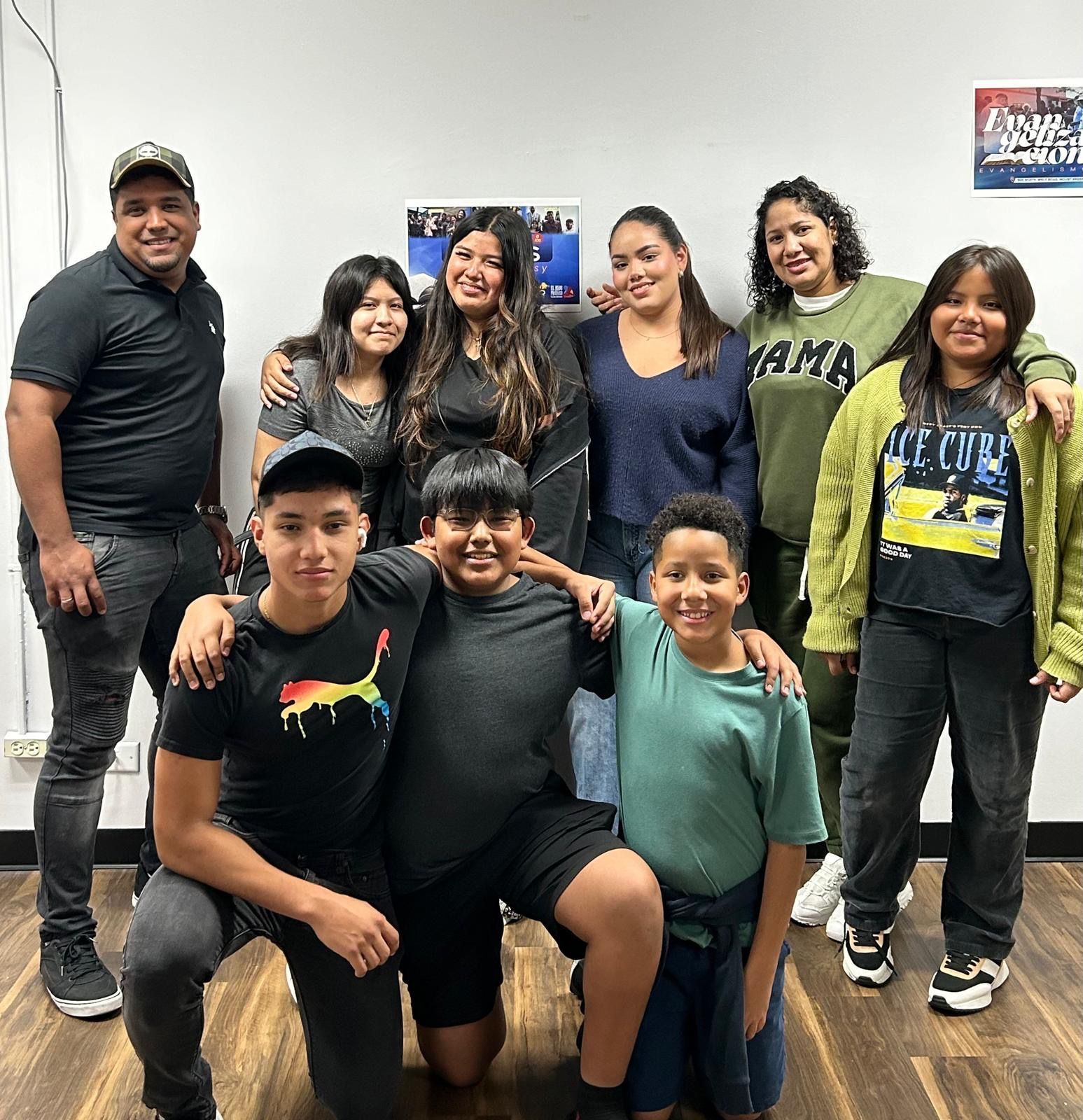 Group of people, indoors, posing together. Some people are kneeling, all are smiling, casual attire.