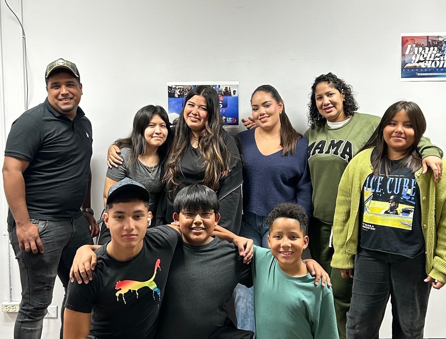 Group of people, indoors, posing together. Some people are kneeling, all are smiling, casual attire.
