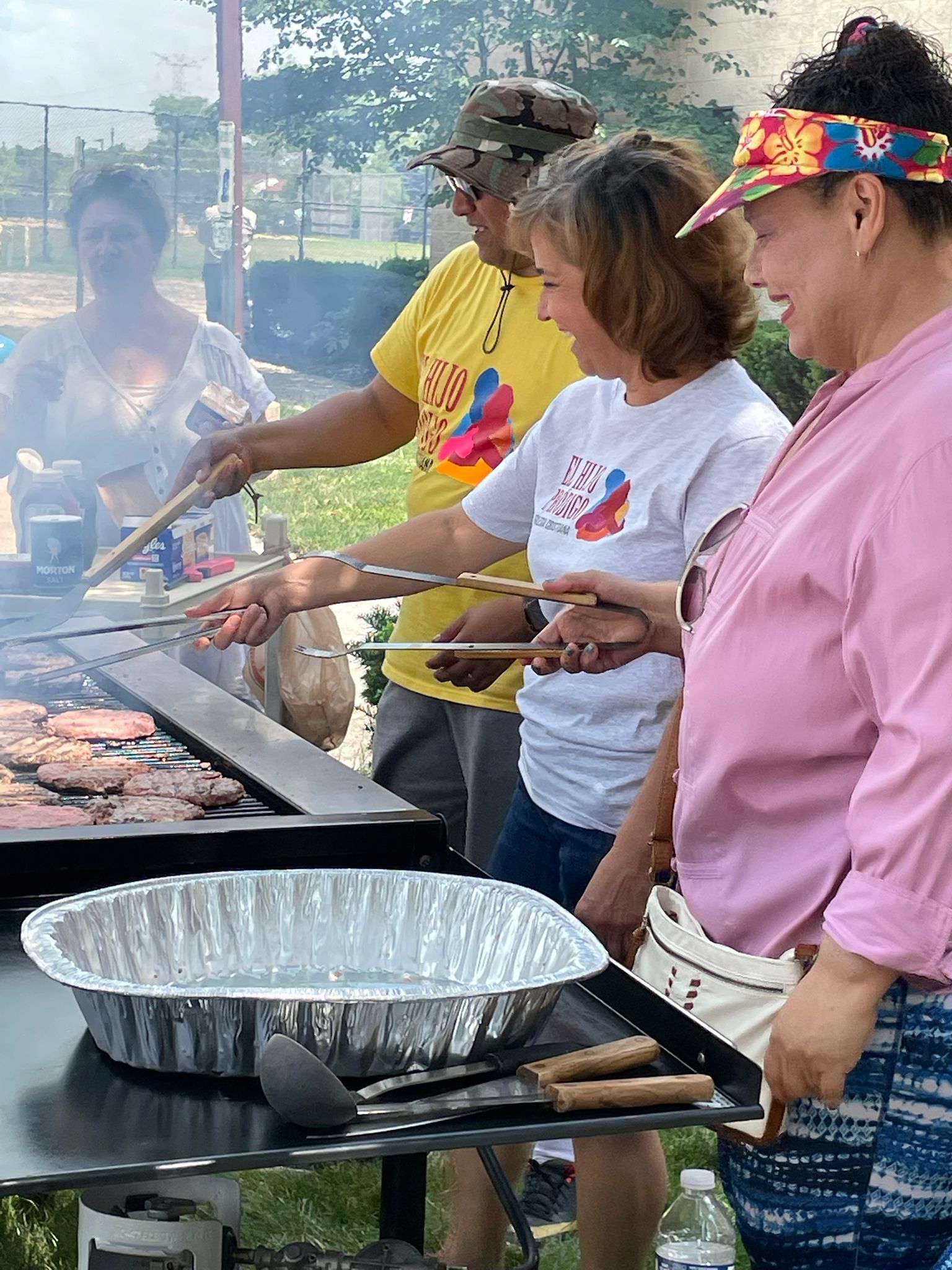 People grilling hamburgers and hotdogs outside.