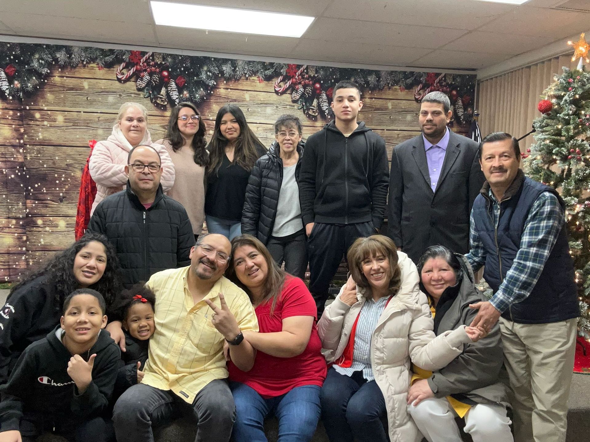 Group of people posing for a photo. Some are smiling in front of a Christmas tree and decorated backdrop.
