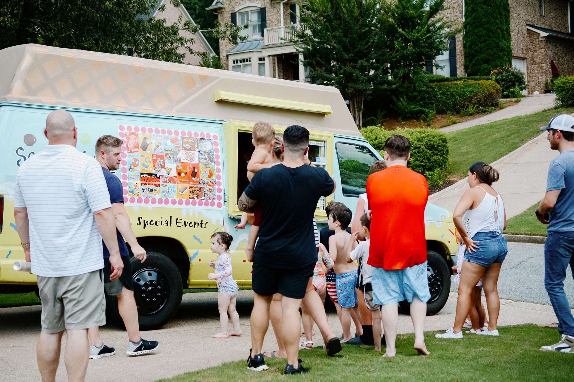 People buying ice cream from a yellow truck parked on a residential street.