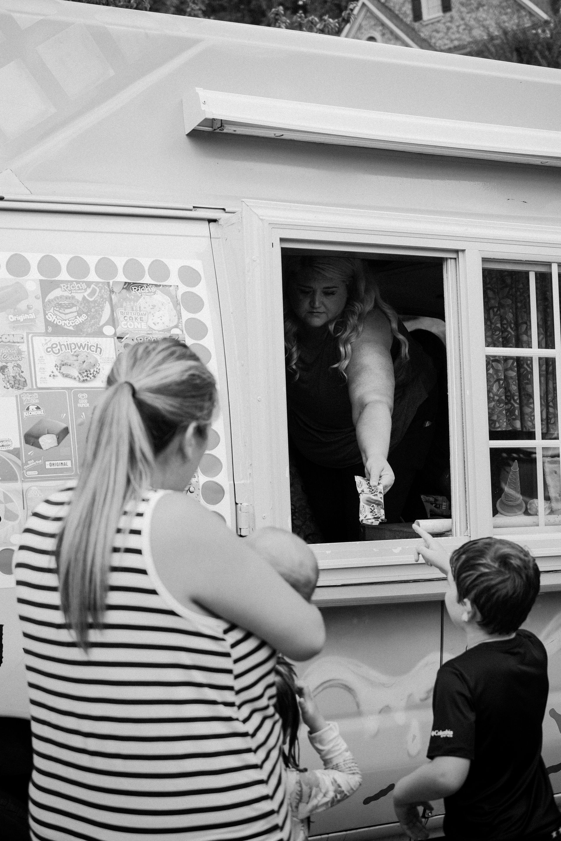 Woman and child buying from a food truck window. Woman in striped shirt watches child reach for item.