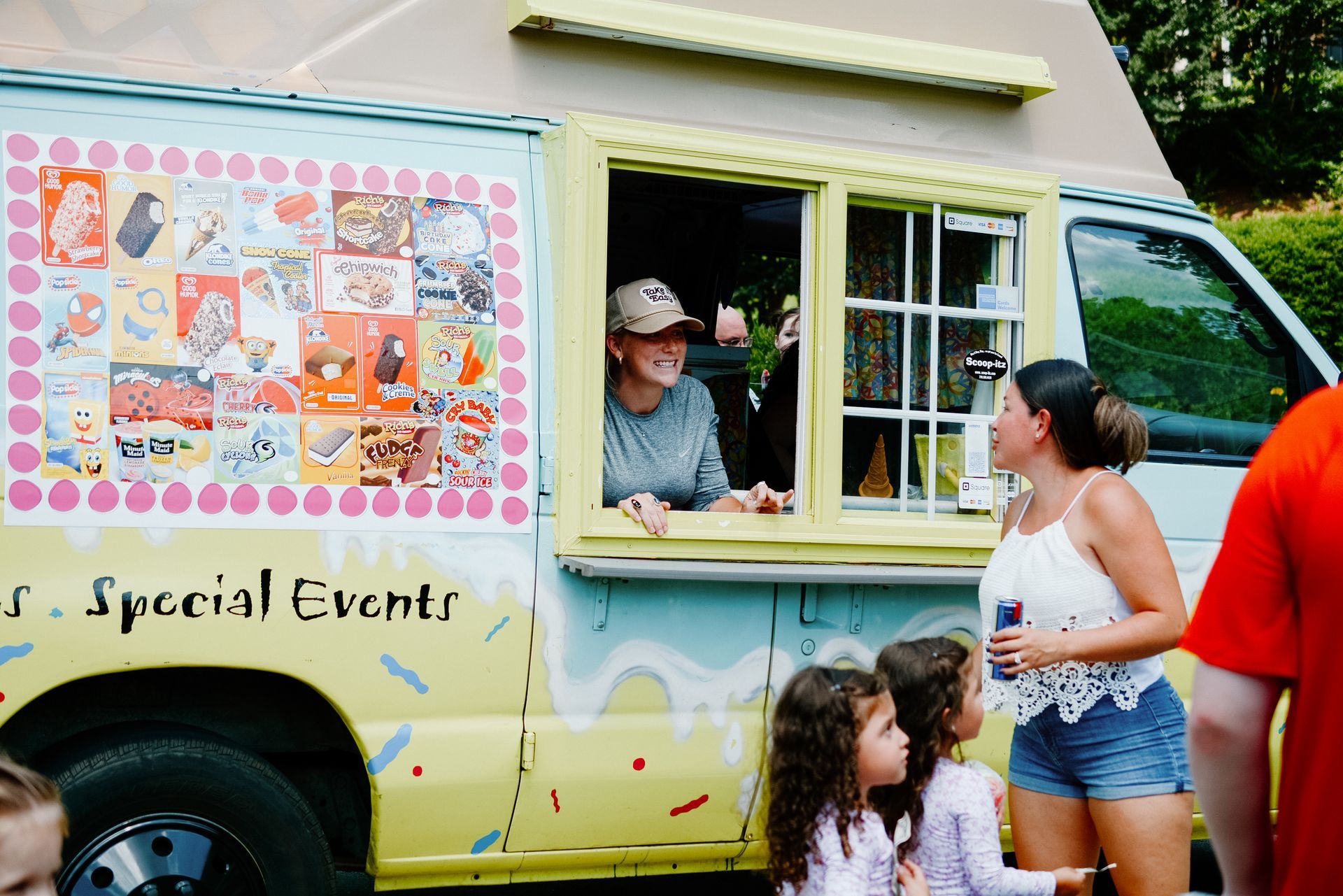 Ice cream truck with a person serving customers at the window. People are waiting.