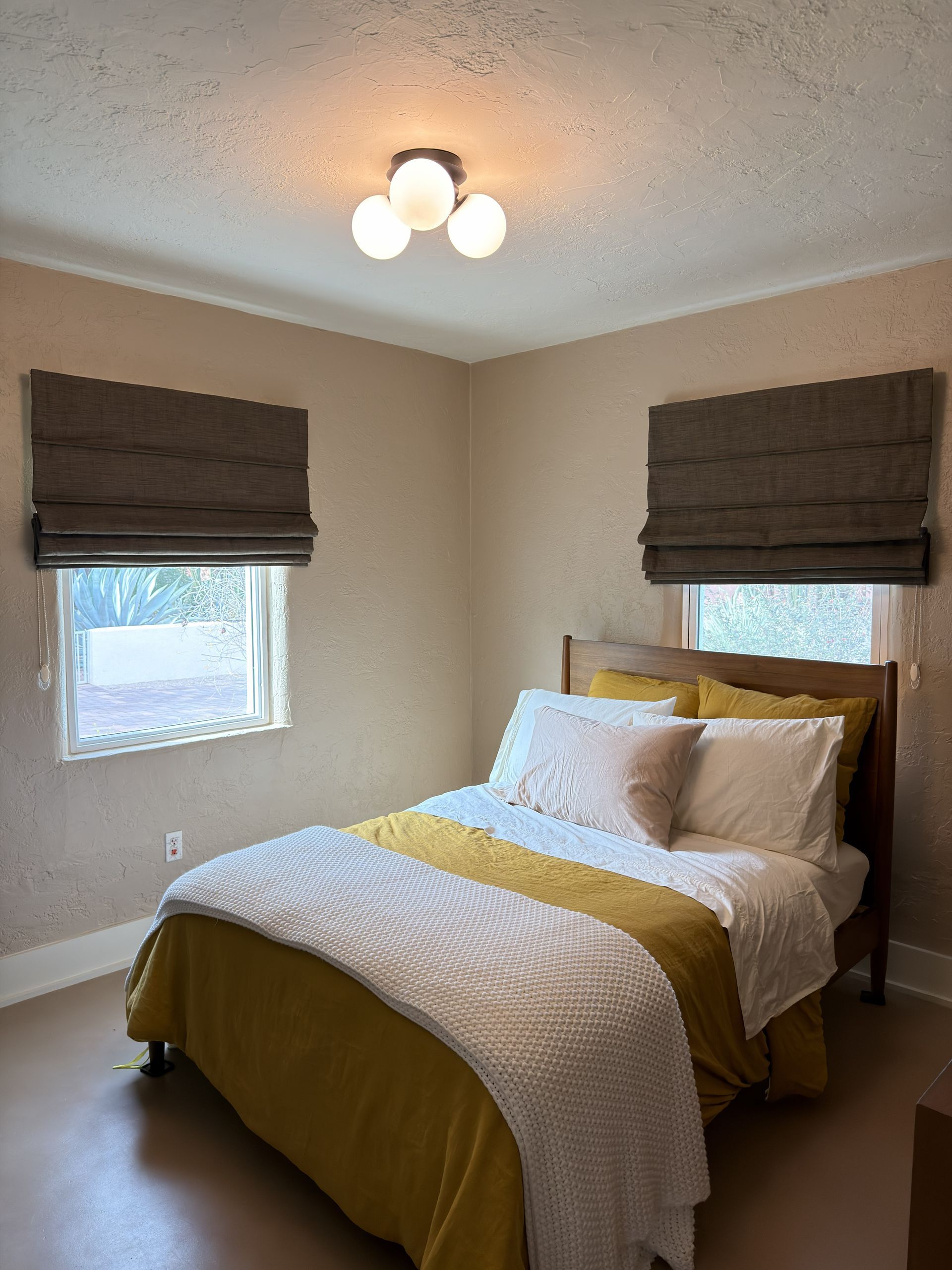 Gray Roman shades over large windows, overlooking a green outdoor area.