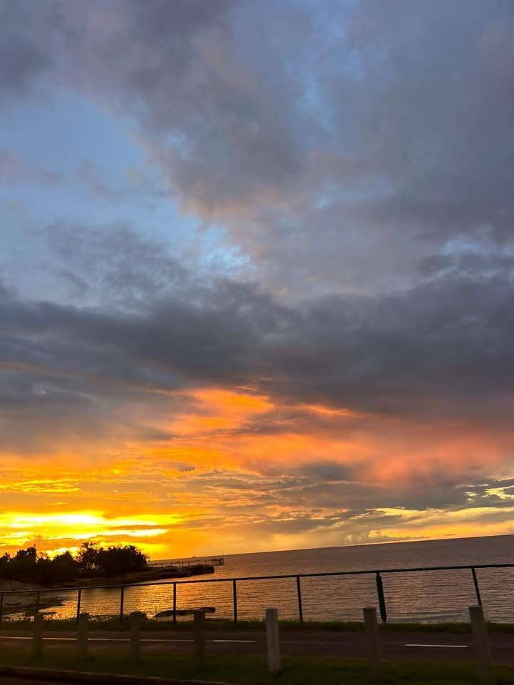 A sunset over a body of water with a fence in the foreground.