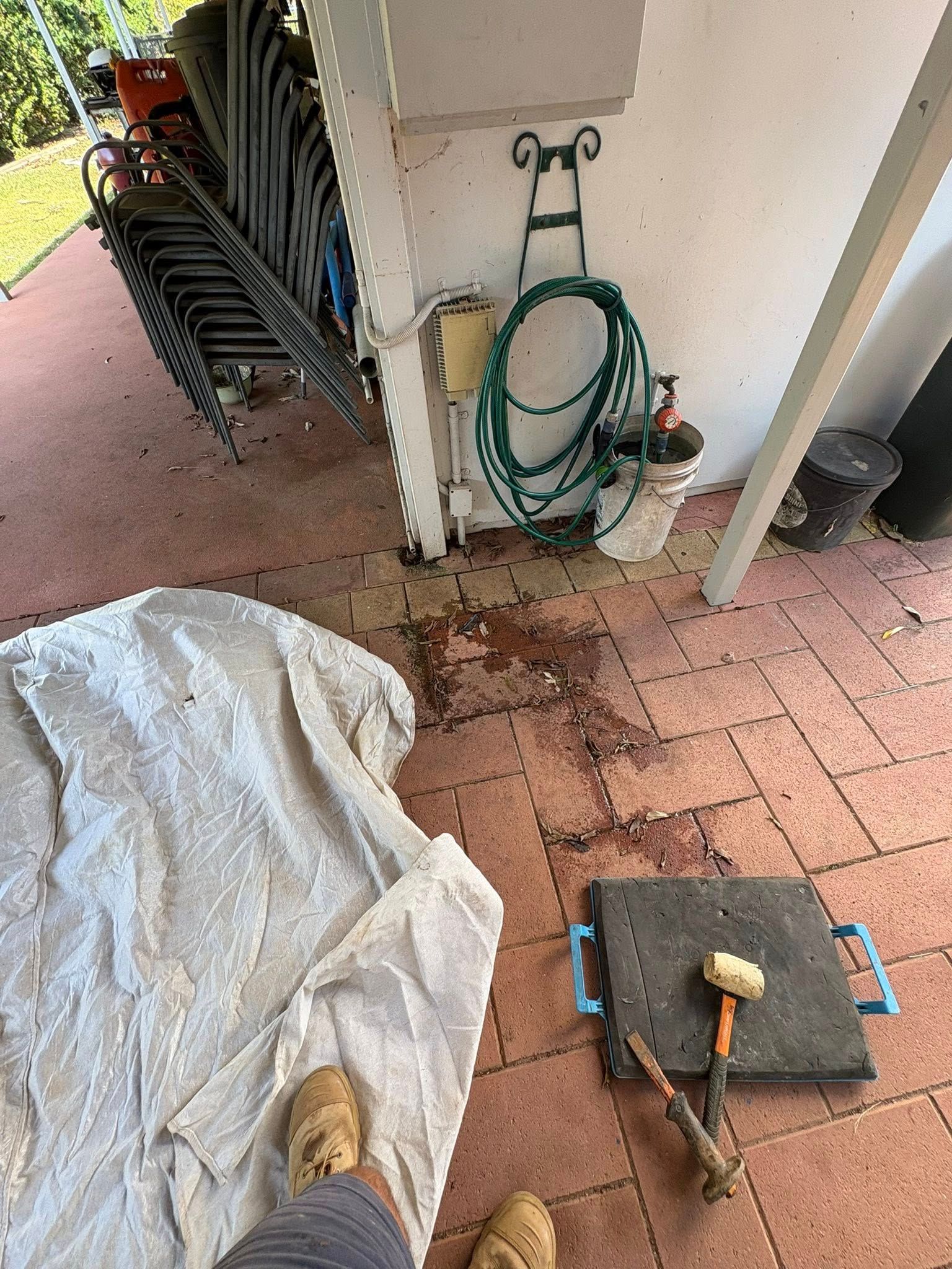 A person is standing on a patio next to a hose and a hammer.